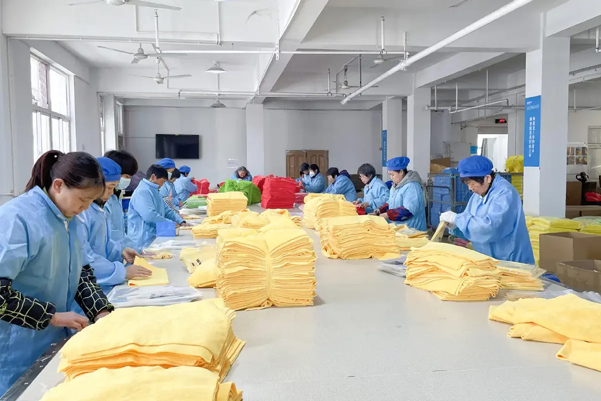 Factory workers inspecting and folding finished yellow hand towels before packing