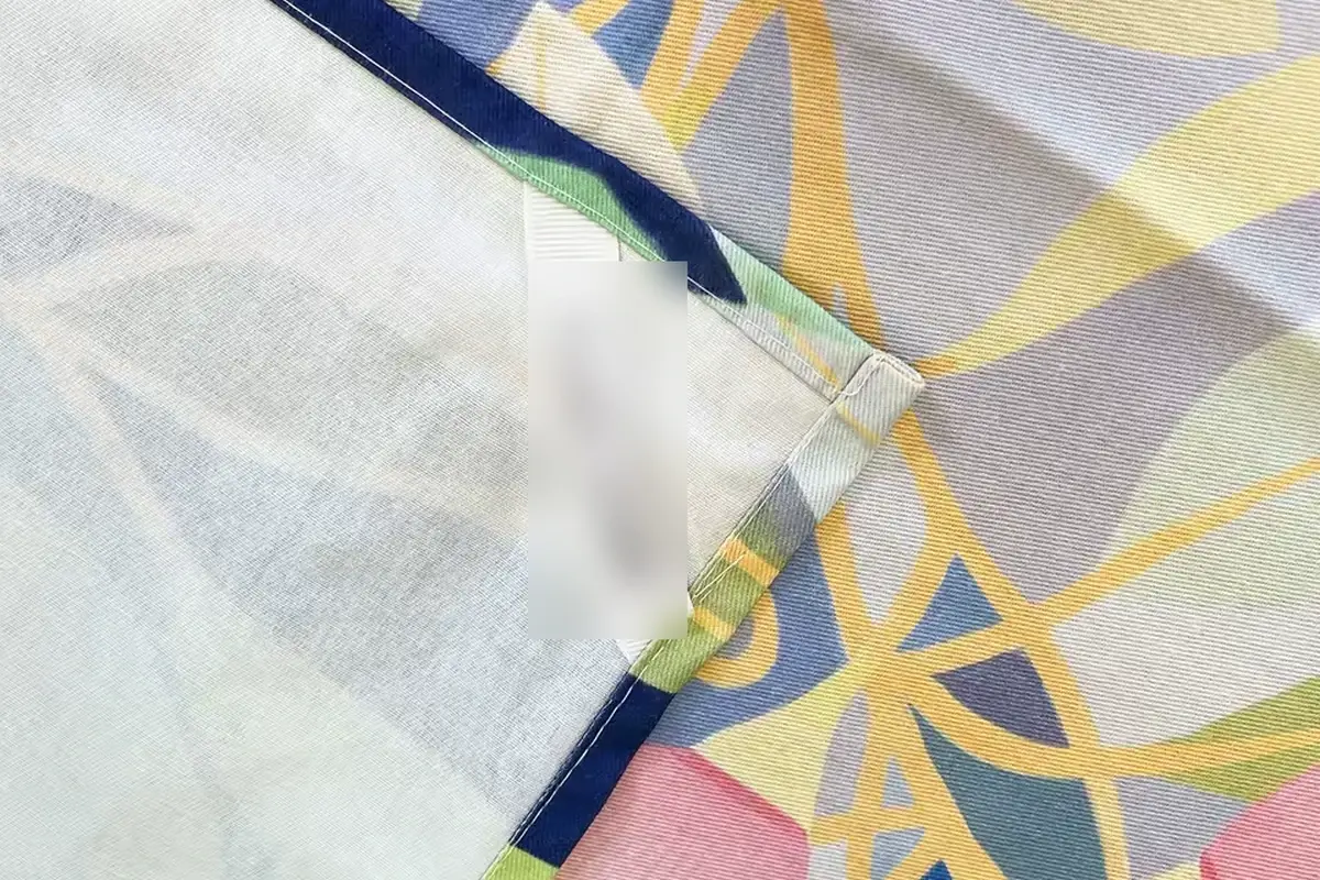 Close view of a sewn fabric label at the finished edge of a printed kitchen towel