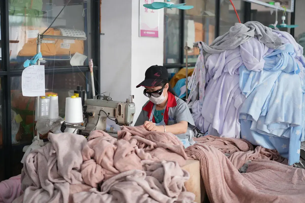 Worker handling towel pieces at a sewing station during finishing quality control